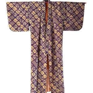 May include: A full-length kimono featuring a repeating geometric diamond pattern in deep purple and cream. The garment has wide sleeves and a structured collar, with a contrasting solid orange lining visible along the front opening and hem.