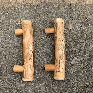 May include: Two wooden cabinet knobs with a natural wood finish and a rough, textured surface. The knobs have a simple, rectangular shape with a small, round knob on the side.