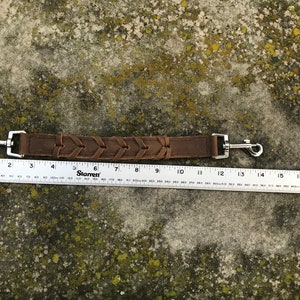 May include: A brown leather dog leash with a braided design and silver metal clips. The leash measures 13 inches long.