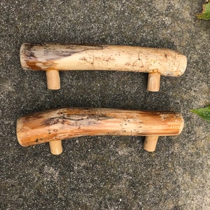 May include: Two wooden handles with a natural finish. The handles are made from a branch of a tree and have been sanded smooth. Each handle has two small wooden knobs on the bottom.
