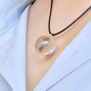 May include: A silver-colored metal object encased in a clear glass sphere pendant on a black cord necklace.