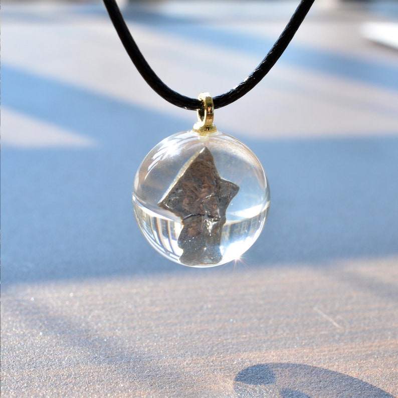May include: A silver-colored star-shaped pendant encased in a clear glass sphere, hanging from a black cord necklace.
