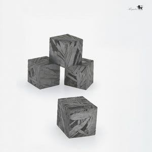 May include: Four dark gray, cube-shaped objects with a patterned surface are arranged against a white background. The cubes appear to be made of a stone-like material, with visible lines and textures. The objects are positioned in a visually appealing arrangement.