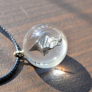May include: A silver-colored meteorite encased in a clear glass sphere pendant on a black cord necklace.