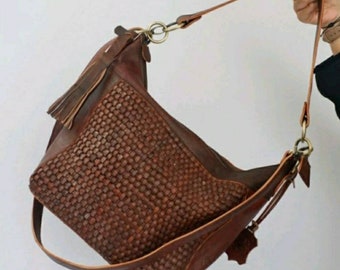 May include: A brown leather woven tote bag with a long adjustable strap and a tassel detail.