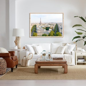 May include: A living room interior with a white sofa, a brown leather armchair, a wooden coffee table, and a framed print of the Eiffel Tower in Paris. The room is decorated with plants and other decorative items.