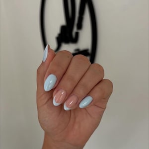 May include: A hand with light blue and French tip oval-shaped acrylic nails. The nails are painted with a pale blue color and a white tip. The nails are well-manicured and have a glossy finish.