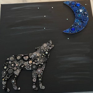 May include: A black canvas painting with a wolf howling at the moon. The wolf and moon are made of buttons in various shades of blue, gray, and black.