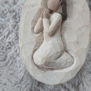 Könnte beinhalten: Eine geschnitzte, ovale Figur einer knienden Person im Gebet. Die Figur trägt ein langes, fließendes weißes Gewand, die Hände gefaltet. Die Figur ist hellbeige mit strukturierter Oberfläche. Maße in cm.