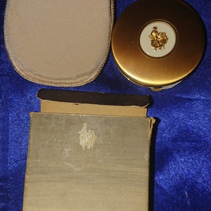 Può includere: Set compatto Yardley vintage, con un compatto dorato con un emblema decorativo, un piumino abbinato e una scatola. La scatola è contrassegnata con "YARDLEY". Il set è probabilmente della metà del XX secolo.