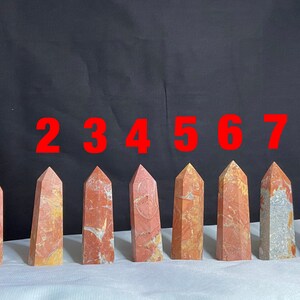 May include: Eight red, orange, and white striped crystal points numbered 1 through 8. The points are arranged in a row on a white surface.