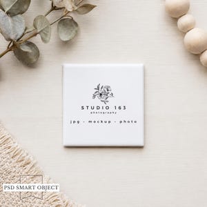 May include: A square, white ceramic tile featuring the text "STUDIO 163 photography" and the words "jpg • mockup • photo" beneath a floral design. The tile is set amongst decorative elements, including eucalyptus leaves and wooden beads.