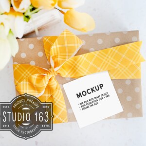 Quadratischer Geschenkanhänger Mockup, quadratischer Beutelbevorzugungsaufkleber-Label-Mockup, Kraftpapier mit gelbem Band, gestylt Stock Photo