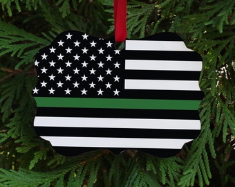 May include: A green line American flag ornament with a red ribbon for hanging. The flag is black, white, and green with a thin green line across the middle.