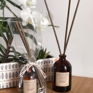 May include: Two brown glass diffuser bottles with wooden reeds. One bottle is wrapped in clear cellophane. Both bottles have labels that read "Diffuseur de parfum BOIS DE OUD Fabrication artisanale."