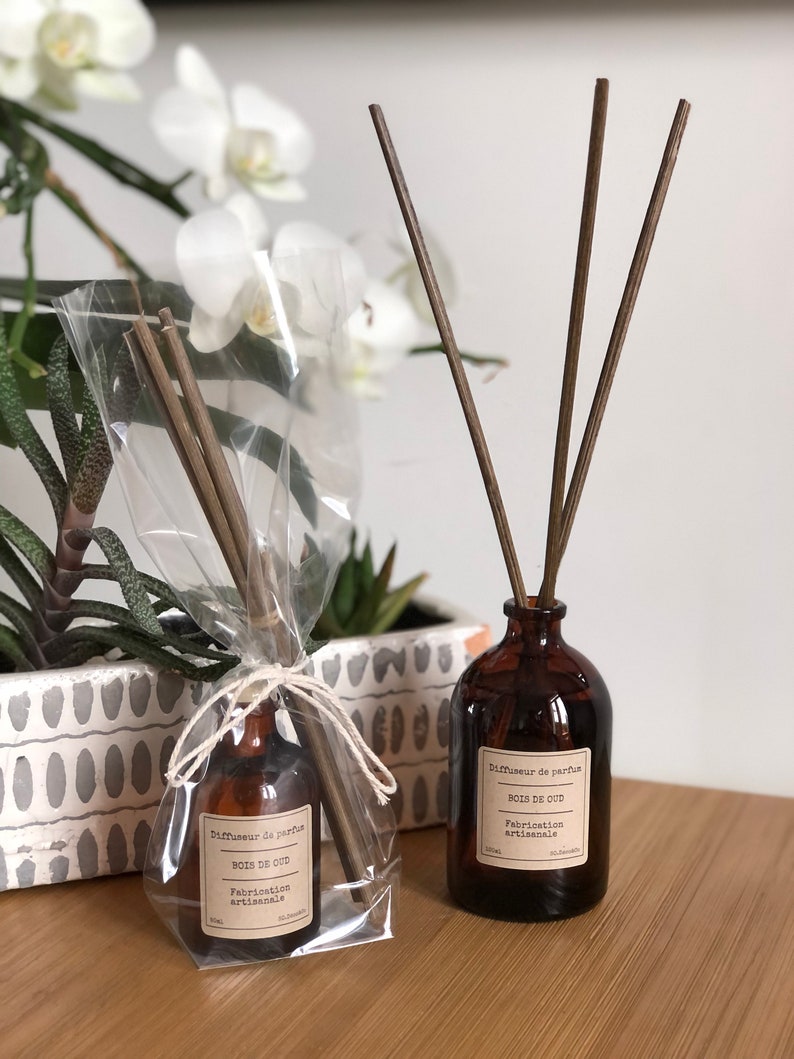 May include: Two brown glass diffuser bottles with wooden reeds. One bottle is wrapped in clear cellophane. Both bottles have labels that read "Diffuseur de parfum BOIS DE OUD Fabrication artisanale."