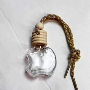 K&ouml;nnte beinhalten: Ein transparenter, apfelf&ouml;rmiger Lufterfrischer f&uuml;r das Auto aus Glas mit einem Holzdeckel und einer gold-braunen Schnur.