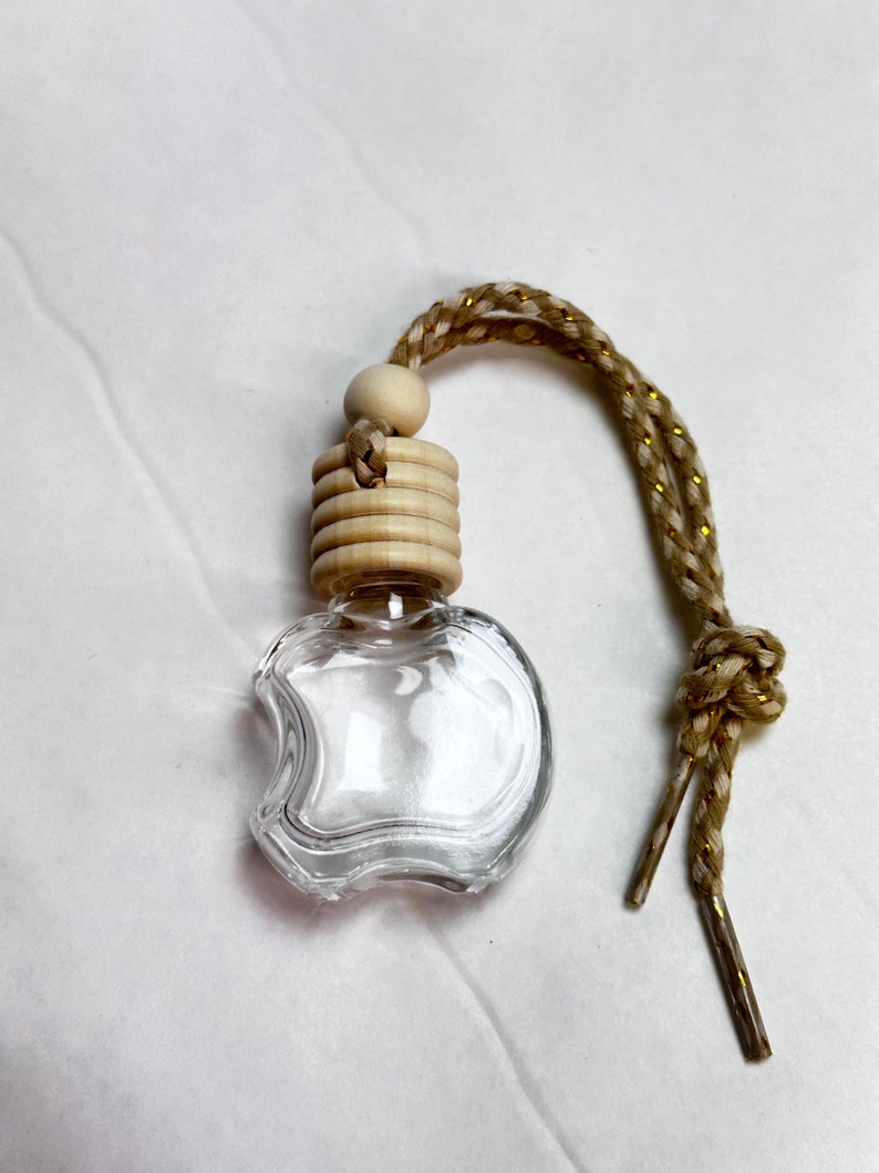 K&ouml;nnte beinhalten: Ein transparenter, apfelf&ouml;rmiger Lufterfrischer f&uuml;r das Auto aus Glas mit einem Holzdeckel und einer gold-braunen Schnur.