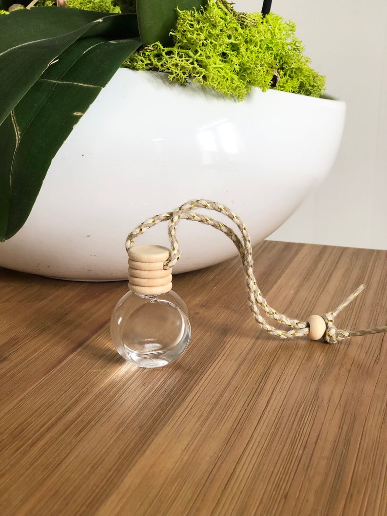 K&ouml;nnte beinhalten: Eine klare Glasflasche mit einem Holzverschluss und einer wei&szlig;en und goldenen Schnur, die daran h&auml;ngt. Die Flasche steht auf einer Holzoberfl&auml;che.