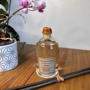 以下が含まれることがあります： 茶色のコルク栓と茶色のラベルが付いた透明なガラス瓶。ラベルには「Diffuseur de parfum, Muguet, Fabrication artisanale, 100ml, So.Decoco.」と書いてあります。