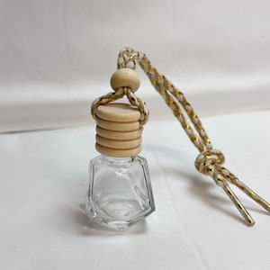 K&ouml;nnte beinhalten: Eine klare Glasflasche mit facettiertem Design, einem Holzverschluss und einer wei&szlig;en und goldenen Schnur zum Aufh&auml;ngen. Die Flasche ist leer und bereit, mit &auml;therischen &Ouml;len oder Duftstoffen gef&uuml;llt zu werden.