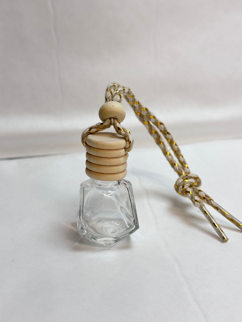 K&ouml;nnte beinhalten: Eine klare Glasflasche mit facettiertem Design, einem Holzverschluss und einer wei&szlig;en und goldenen Schnur zum Aufh&auml;ngen. Die Flasche ist leer und bereit, mit &auml;therischen &Ouml;len oder Duftstoffen gef&uuml;llt zu werden.