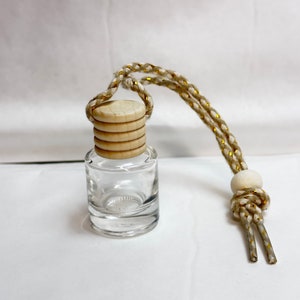 K&ouml;nnte beinhalten: Eine klare Glasflasche mit einem Holzverschluss und einer wei&szlig;en und goldenen Schnur. Die Flasche ist leer und bereit, mit &auml;therischen &Ouml;len oder anderen Fl&uuml;ssigkeiten gef&uuml;llt zu werden.