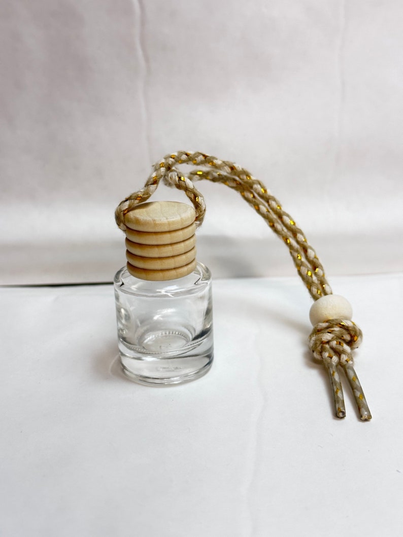 K&ouml;nnte beinhalten: Eine klare Glasflasche mit einem Holzverschluss und einer wei&szlig;en und goldenen Schnur. Die Flasche ist leer und bereit, mit &auml;therischen &Ouml;len oder anderen Fl&uuml;ssigkeiten gef&uuml;llt zu werden.