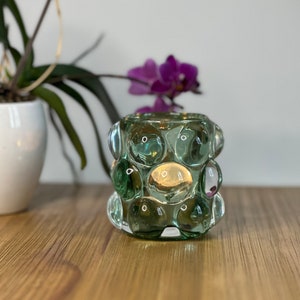 Op de afbeelding: Een groene glazen kaarsenhouder met een textuur van bubbels. De houder staat op een houten oppervlak.