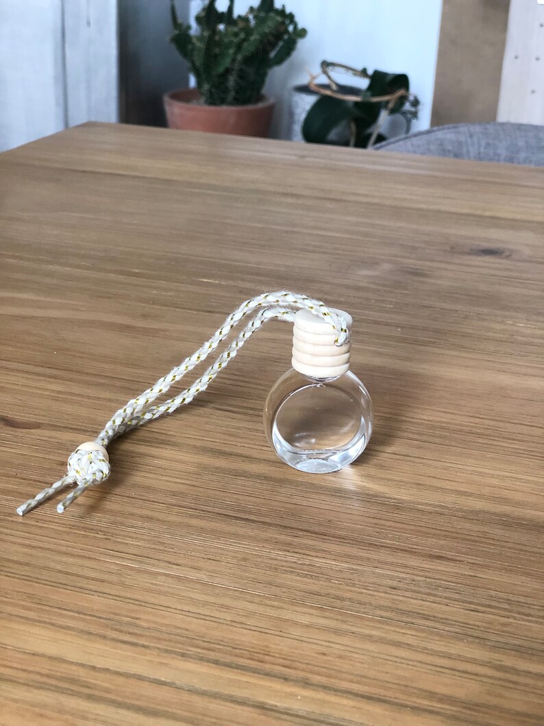 K&ouml;nnte beinhalten: Eine klare Glasflasche mit einem Holzverschluss und einer wei&szlig;en und goldenen Schnur. Die Flasche steht auf einer Holzoberfl&auml;che.