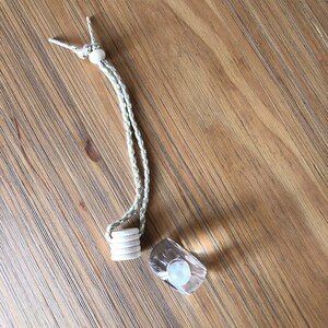 K&ouml;nnte beinhalten: Ein wei&szlig;es Band mit einer Holzperle oben und einem Stapel Holzringe unten. Neben dem Band befindet sich eine durchsichtige Glasflasche mit einem wei&szlig;en Verschluss.