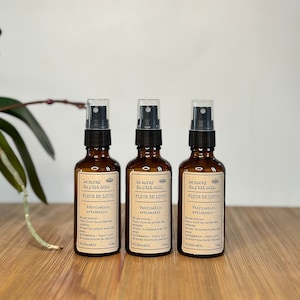 May include: Three brown glass spray bottles with black spray tops. Each bottle is labeled "Le spray du p'tit coin" and "FLEUR DE LOTUS". The bottles are on a wooden surface.