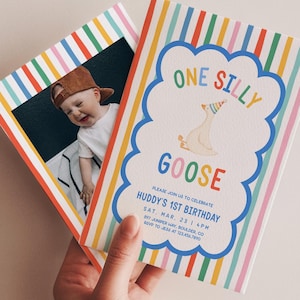 May include: Two colorful birthday invitations are held in a hand. One invitation features a photo of a baby wearing a cap. The other invitation has the text "ONE SILLY GOOSE" in a cloud-shaped design, with the event details below.