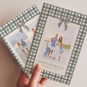 May include: Two holiday greeting cards with family photos. The cards have a gray and white gingham border and a decorative bow. The text "HAPPY HOLIDAYS" and family name are printed on the front of the card.
