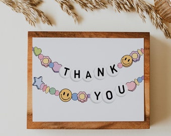 May include: A wooden frame with a white card inside. The card has a colorful garland with smiley faces, hearts, and stars. The garland spells out "THANK YOU".