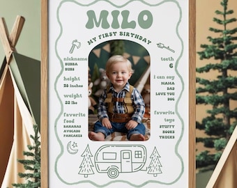 Peut inclure: Un chevalet en bois présente un panneau de jalon pour le premier anniversaire d'un enfant. Le panneau présente le nom "Milo" en vert, ainsi que la photo de l'enfant, sa taille (61 cm), son poids (14,5 kg) et ses choses préférées. Le panneau est décoré d'illustrations sur le thème du camping.