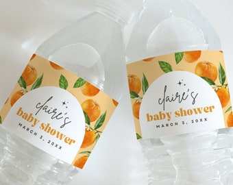 May include: Two clear plastic water bottles with orange and green floral labels. The labels say "Claire's baby shower" with a date.