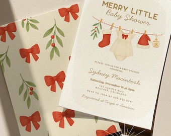 May include: A baby shower invitation with a festive design. The invitation features the text "MERRY LITTLE Baby Shower" and includes illustrations of baby clothes and holiday decorations. The envelope has a pattern of red bows and green leaves.