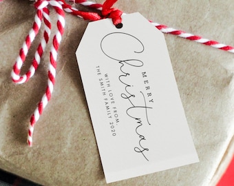 Könnte beinhalten: Eine braune Geschenkbox, die mit rot-weißem Garn umwickelt ist und ein weißes Geschenkanhänger mit der Aufschrift "Frohe Weihnachten" mit Liebe von der Familie Smith 2020.