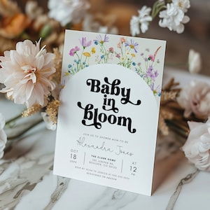 May include: A white baby shower invitation with a floral border and the text "Baby in Bloom" in a black retro font. The invitation includes the date, time, and location of the shower for Alexandra Jones.