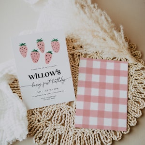 May include: A pink and white gingham patterned card with the text "PLEASE JOIN US TO CELEBRATE WILLOW'S berry first birthday SAT JUL 9 2PM 125 JUNIPER PLUM WAY | SANTA CRUZ, CA RSVP TO JESSICA 800.200.9000" on a white card with a strawberry illustration.