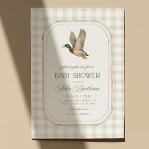 May include: Baby shower invitation with a flying duck illustration. The invitation features the text "please join us for a BABY SHOWER in honor of Mila Bartleson". The date and time are August 15 at 2 PM. The invitation is on a beige and white checkered background.