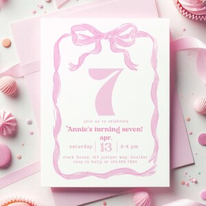May include: Pink invitation card with a large pink number seven and a pink bow. The text on the card reads 'join us to celebrate 'Annie's turning seven!' apr. 13 2-4 pm clark house. 123 juniper way, boulder rsvp to kelly at 123.456.7890'