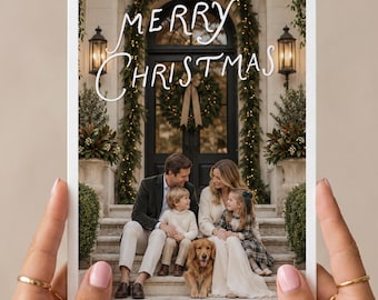 Peut inclure: Une carte de vœux rectangulaire avec le texte blanc Merry Christmas. L'image montre une famille de trois personnes et un golden retriever assis sur des marches en pierre devant une porte arquée sombre ornée de guirlandes et d'une couronne.