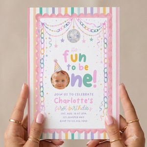 K&ouml;nnte beinhalten: Eine rechteckige Geburtstagseinladungskarte mit pastellfarbenem Streifenrand, einer Discokugel und bunten Papierketten. Der Text lautet: It's fun to be one! Join us to celebrate Charlotte's first birthday, Sat, Aug, 10 at 2pm, 123 Juniper Way, RSVP to 123.456.7890.