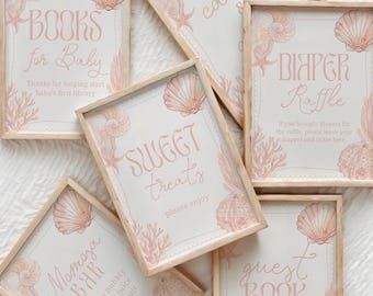 May include: A collection of framed signs with a seashell and coral theme. The signs have a light pink and beige color scheme and include text such as "Books for Baby", "Sweet Treats", and "Guest Book". The frames are made of light wood.