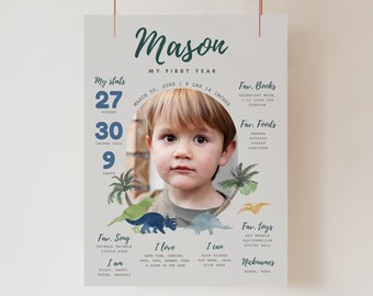 May include: A personalised first birthday chart for a boy named Mason. The chart features a photo of the boy, his stats, favourite foods, books, songs, toys, and activities. The chart is decorated with a dinosaur theme and has a green, blue, and white colour scheme.