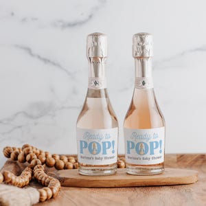 May include: Two mini bottles of champagne with blue and white labels that say "Ready to POP!" and "Marissa's Baby Shower".