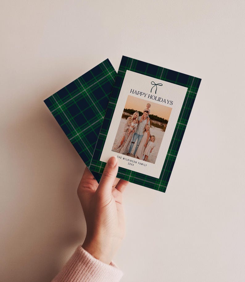 May include: A holiday card with a family photo, featuring a green and navy plaid pattern border. The card reads "HAPPY HOLIDAYS" with a bow graphic. The family photo is on a white background.