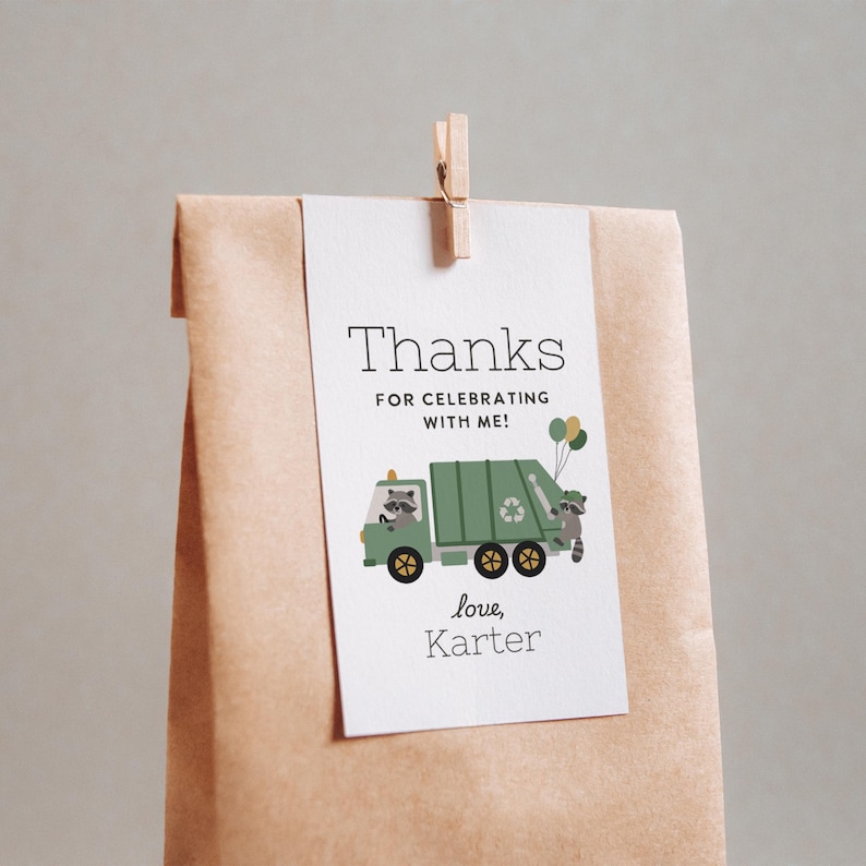 May include: A white tag with the text "Thanks FOR CELEBRATING WITH ME!" is clipped to a brown paper bag. The tag features a green garbage truck with a raccoon driver and a raccoon holding balloons. The text "love, Karter" is below.